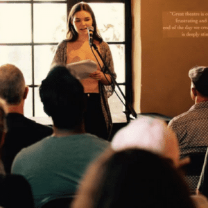 A teen girl reads her story in front of an audience.