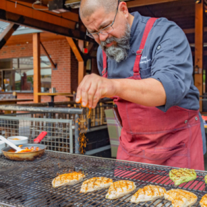 A man in a red apron grills chicken. This is for a Memorial Day roundup.