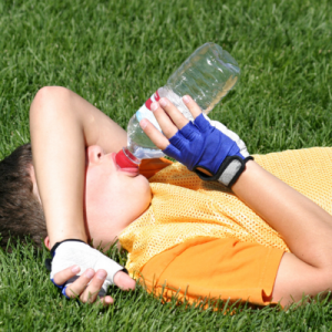 Young boy lies on grass, drinking bottled water for a story on preventing sports burnout in kids.